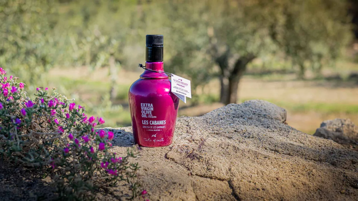 Botella de aceite de oliva virgen extra Les Cabanes sobre una roca entre olivos