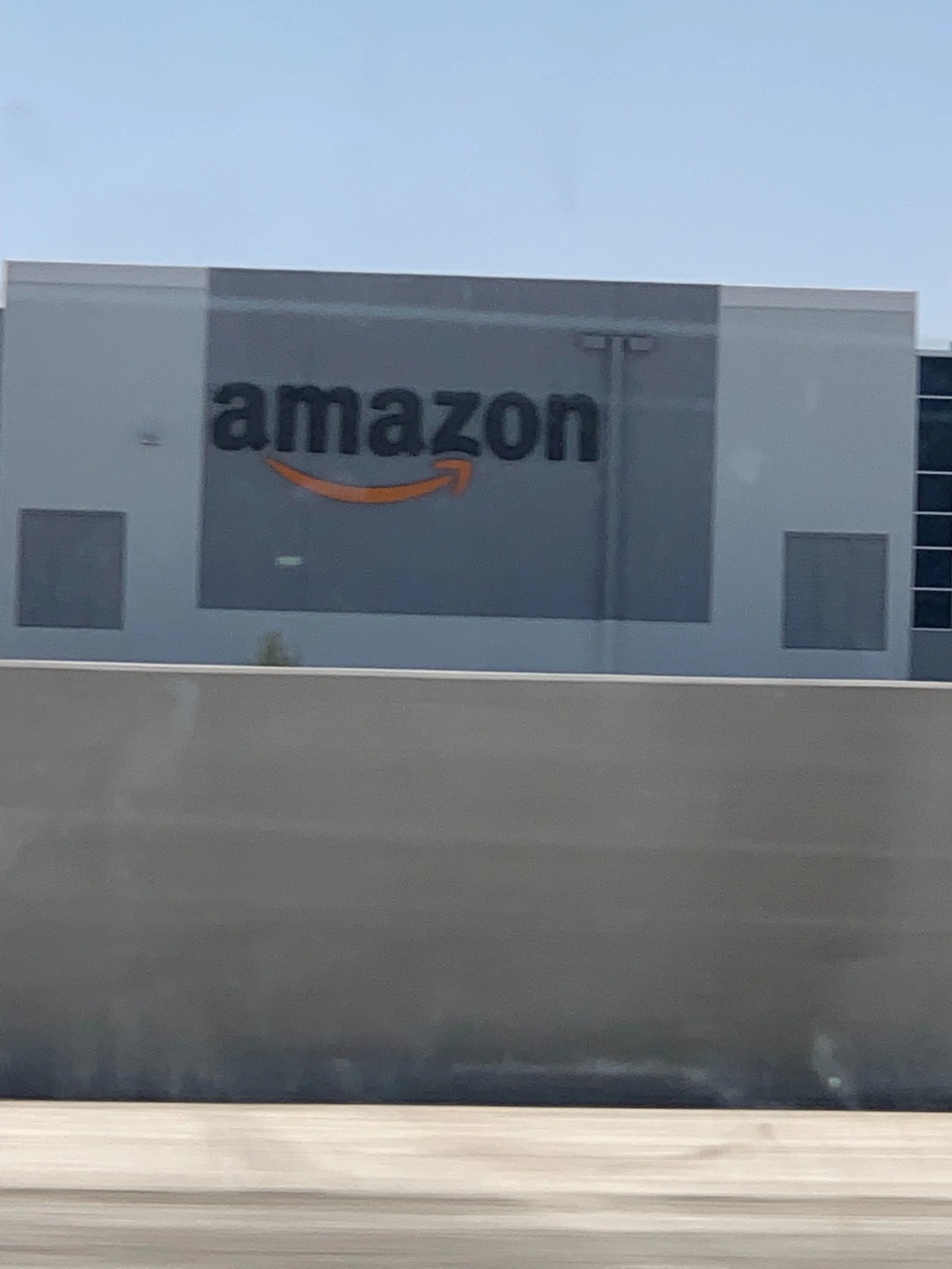 Logo de Amazon en el exterior de un centro de fulfillment con camiones de reparto y cielo despejado